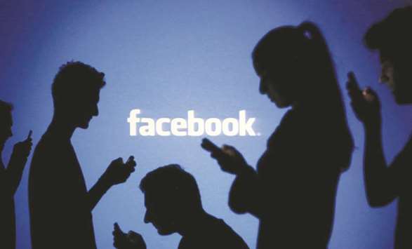 People are silhouetted as they pose with mobile devices in front of a screen projected with a Facebook logo in New York. China has withdrawn its approval for Facebooku2019s  plan to open a new venture in the eastern province of Zhejiang, the New York Times reported on Wednesday, citing a person familiar with the matter.