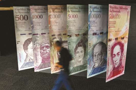In this file photo taken on January 31, 2018 a man walks past banners depicting Venezuelau2019s currency, the bolivar, at the Central Bank of Venezuela (BCV) in Caracas. According to an IMF projection that poses volatile scenarios, inflation in Venezuela would reach 1,000,000% this year, with a single certainty: the dramatic deterioration of living conditions.