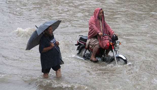 A man holds an umbrella as he walks through floodwaters during heavy rain in Lahore