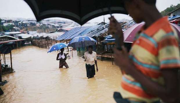 Rohingya refugees walk along the water as parts of the Kutupalong camp flooded during heavy rain in Cox's Bazar, Bangladesh,