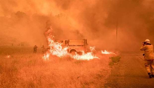 Firefighters scramble to control flames surrounding a fire truck as the Pawnee fire jumps across highway 20 near Clearlake Oaks, California.
