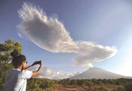 A woman takes photos as Mount Agung volcano sends up another plume of smoke, seen from the Kubu subdistrict in Karangasem Regency on Indonesiau2019s resort island of Bali.