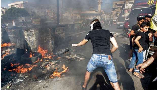 A masked man throws a tire into a fire as protesters block the main road outside the Palestinian refugee camp of Burj al-Barajneh, south of the Lebanese capital Beirut