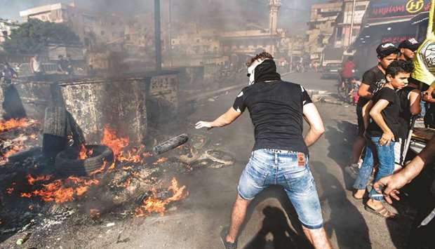 A masked man throws a tire into a fire as protesters yesterday blocked the main road outside the Palestinian refugee camp of Burj al-Barajneh, south of the Lebanese capital Beirut.