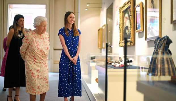 Britain's Queen Elizabeth II looks at a dress worn by Albert Edward, Prince of Wales (later King Edward VII) alongside Lucy Peter, assistant curator, as part of an exhibition to mark the 200th anniversary of the birth of Queen Victoria, for the Summer Opening of Buckingham Palace in London