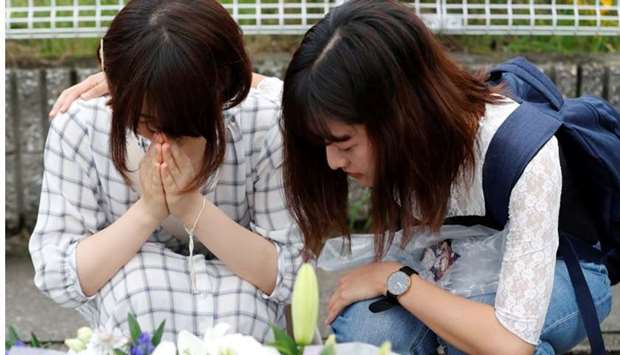 Women pray in front of a row bouquets placed out for victims of the torched Kyoto Animation building in Kyoto, Japan