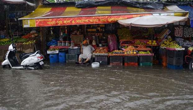 A vendor sits under cover at his flooded fruit shop during heavy monsoon rain in Amritsar yesterday.