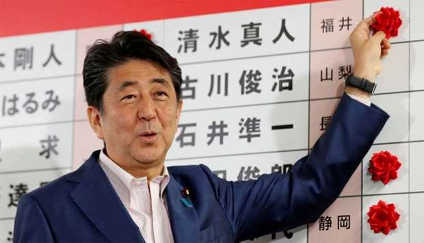 Japan's Prime Minister Shinzo Abe puts a rosette on the name of a candidate who is expected to win the upper house election at the LDP headquarters in Tokyo