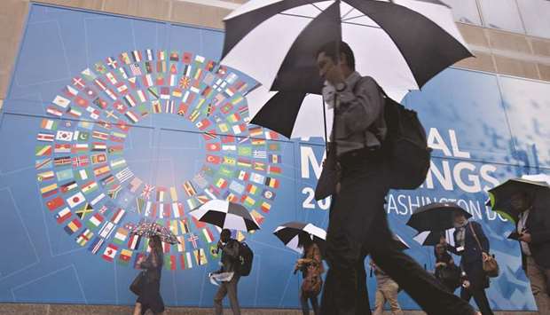 Pedestrians hold umbrellas while walking past a sign for the IMF and World Bank Group Annual Meetings in Washington, DC in October 2017.