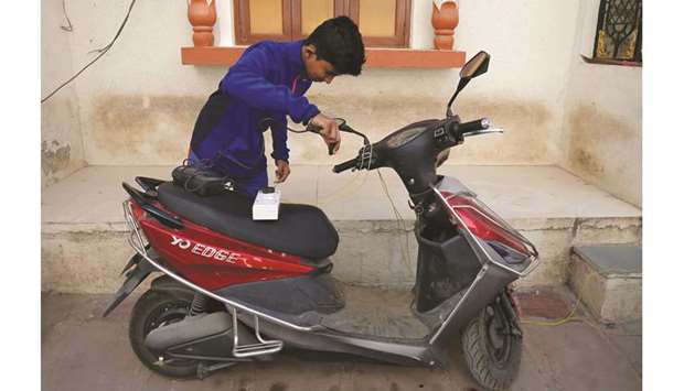 FILE PHOTO: A boy prepares to recharge his electric scooter outside his home in Ahmedabad, India.