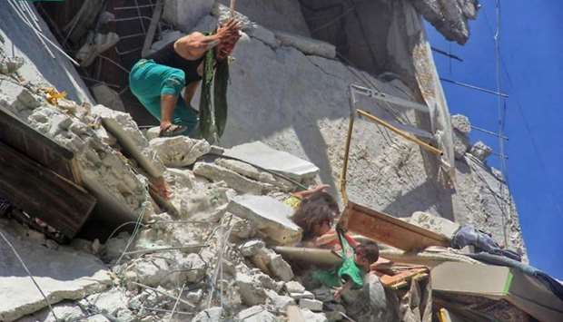 An image grab taken from a video by Syrian news website SY24 on July 25, 2019 shows a Syrian man reacting as two dust-covered Syrian girls, trapped in rubble, grab their baby sister from her shirt as she dangles from a bombed-out building in the Syrian town of Ariha in the northwestern province of Idlib. AFP/SY24/Bashar al-Sheikh