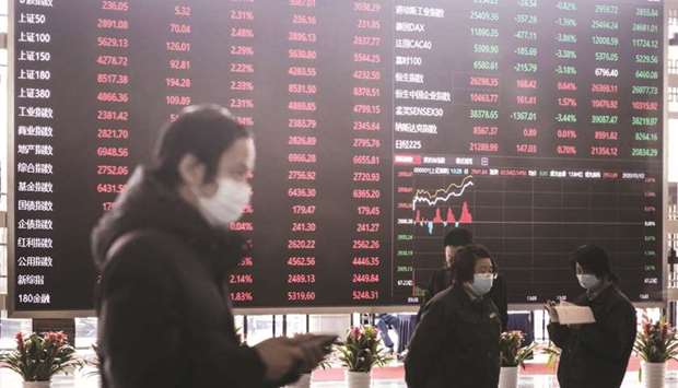 Employees and visitors wearing protective masks walk past an electronic stock board at the Shanghai Stock Exchange. The Composite index closed down 2.0% to 3,383.32 points yesterday.