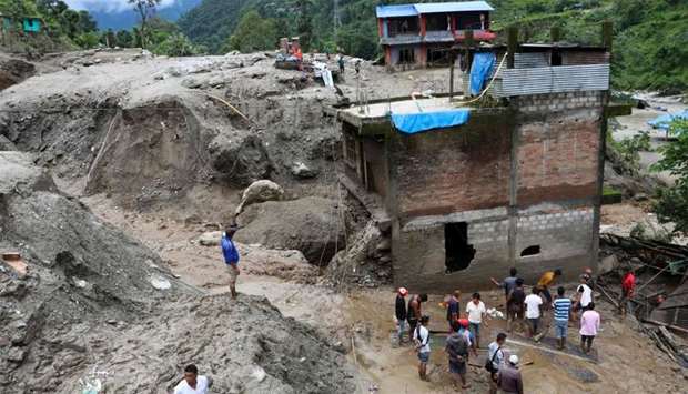 Residents and rescue workers inspect the area outside a house damaged by a landslide and the swell of the Thado-Koshi river due to heavy rains in Jambu village of Sindhupalchok district, some 80 kms northeast of Kathmandu