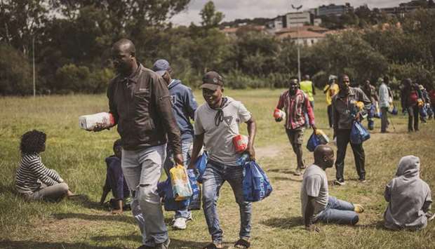 Homeless persons carry their food parcels as they walk past others queuing in Innesfree Park in Johannesburg on April 9. With gross domestic product expected to shrink as much as 10% this year due to a lockdown to curb the spread of Covid-19, a common vision and decisive leadership are needed more urgently than ever, according to Business Unity South Africa, which forms part of B4SA.