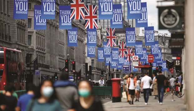 People walk underneath Union Jack flags and banners with a message reading u201cThank you #ourheroesu201d as restrictions are eased following the outbreak of the coronavirus disease in Regent Street, London.