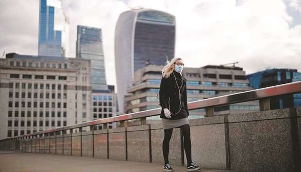 A woman wearing a face mask, walks across London Bridge away from the City of London. Britainu2019s economy slumped by almost a fifth in the three months to May compared with the prior December-February period, as the coronavirus lockdown ravaged activity, official data showed yesterday.