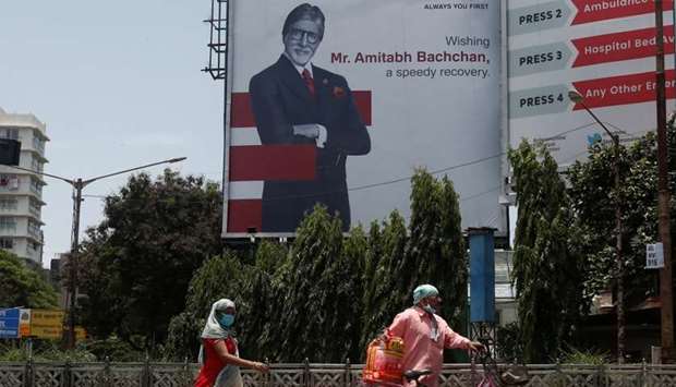 People wearing protective masks walk in front of a hoarding of Bollywood actor Amitabh Bachchan wishing him a speedy recovery in Mumbai. Bachchan and members of his family who tested positive for coronavirus disease are under treatment in a Mumbai hospital.