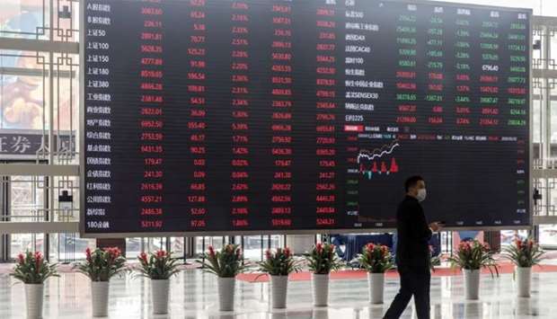 A man wearing a protective mask walks past an electronic stock board at the Shanghai Stock Exchange. The Composite index closed up 3.1% to 3,314.15 points