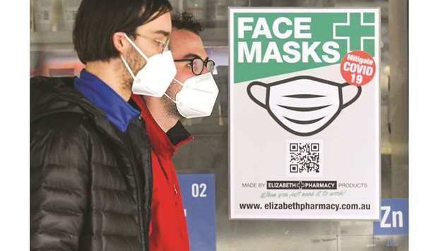 People wearing face masks walk past a sign advertising masks in Melbourne yesterday.