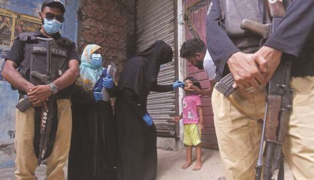 Policemen stand guard as a health worker (centre) administers polio vaccine drops to a child during a polio vaccination door-to-door campaign in Karachi yesterday.