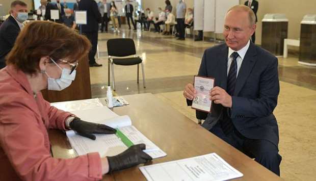 Russian President Vladimir Putin shows his passport to a member of a local electoral commission as he arrives to cast his ballot at a polling station in Moscow.