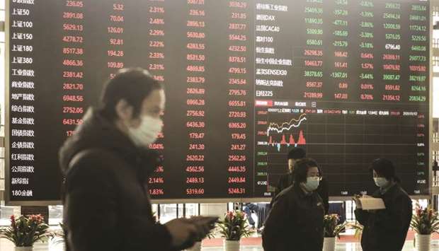 Employees and visitors wearing protective masks walk past an electronic stock board at the Shanghai Stock Exchange. Shanghai stocks fell 0.2% to 3,325.11 points yesterday.