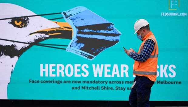 An essential worker wearing a face mask walks past a 'Heroes Wear Masks' sign in Melbourne