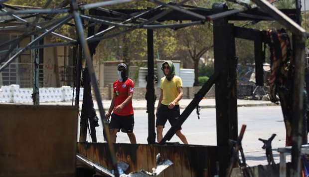Two Iraqi youths walk past the remains of a protest tent, which was burnt the previous night in Baghdad's Tahrir Square