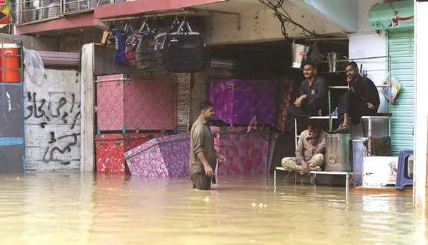 Shopkeepers sit outside a shop submerged with water after heavy monsoon rains in Karachi yesterday.