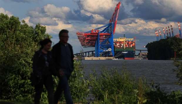 People walk on trail as a container ship sits moored at the HHLA Container Terminal Burchardkai at the Port of Hamburg.