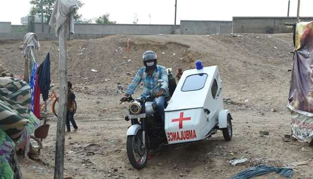 A man drives his motorcycle with its sidecar converted into an ambulance, in a slum area of Ahmedaba
