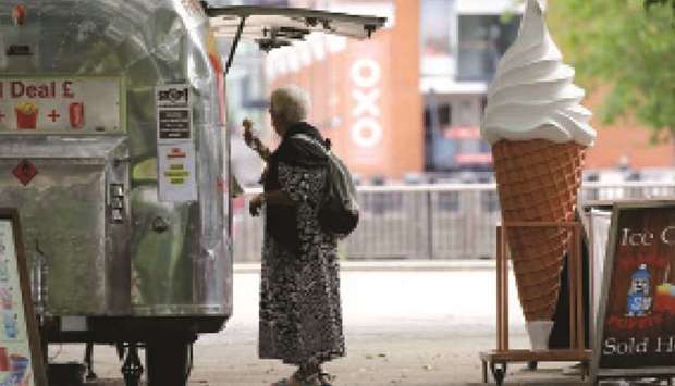 A woman buys an ice-cream at Gabrielu2019s Wharf beside the River Thames in London yesterday. The government has been easing stay-at-home orders imposed in late March with pubs, restaurants and museums reopening today.