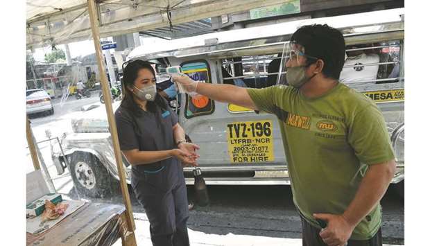 A jeepney driver (right) takes the temperature of a passenger in Manila yesterday, after thousands of jeepneys hit the road again after over three months since they were forced to stop operation amid the Covid-19 coronavirus pandemic.