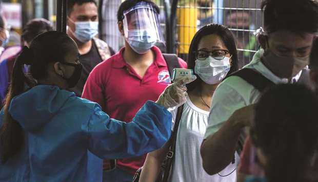 A train passenger has her body temperature taken before boarding a bus at a train station in Manila, yesterday, after authorities suspended operation of one of the train lines after some of its staff tested positive for Covid-19 disease.