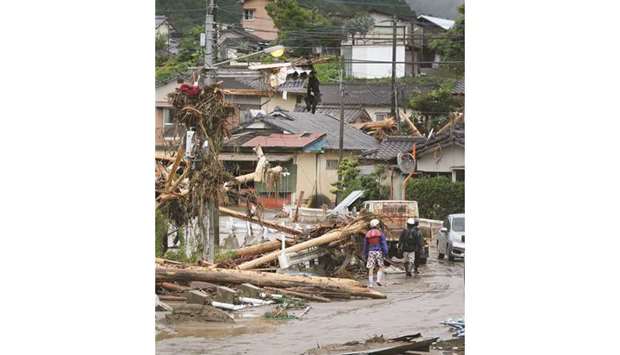 People walk past flood damaged houses and debris following a torrential rain in Kuma, Kumamoto prefecture.
