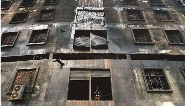 A firefighter stands at a first floor window of the burnt factory in Rupganj after putting out the remnants of a fire yesterday.