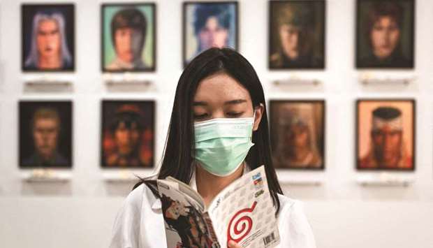 Thai artist Jinnipha Nivasabut reading the Japanese manga Naruto by Mavashi Kishimoto. In the background are oil portraits of deceased anime characters, at her exhibition The 2D Afterlife, at Palette Artspace in Bangkok.