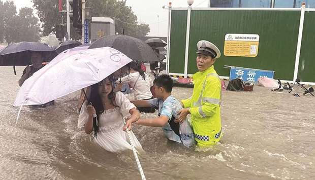 A traffic police officer guides residents to cross a flooded road with a rope during heavy rainfall in Zhengzhou.