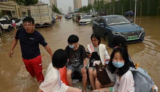 People ride on a rubber boat to cross a flooded street following heavy rain that flooded and claimed the lives of at least 33 people earlier in the week, in the city of Zhengzhou, in China's Henan province