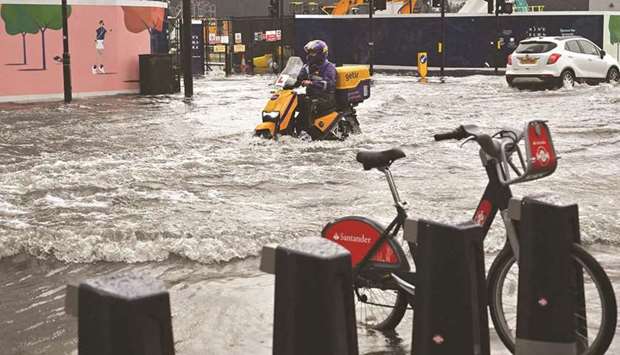 A motorcyclist rides through deep water on a flooded road in The Nine Elms district of London.