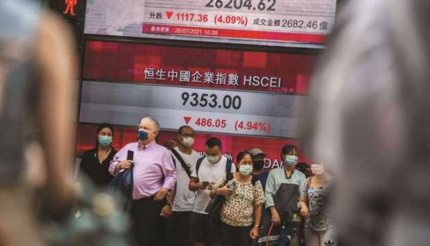People stand in front of an electronic display showing the Hang Seng Index in the central district of Hong Kong on July 26 after stocks plunged as tuition firms were hammered by Chinau2019s decision to reform the private education sector by preventing them from making profits. Chinau2019s securities regulator convened a virtual meeting with executives of major investment banks on Wednesday night, attempting to ease market fears about Beijingu2019s crackdown on the private education industry.