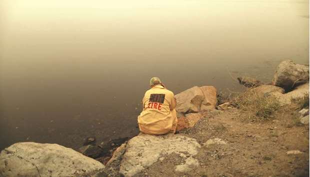 A first responder takes a break as ash from the Dixie Fire falls over the Round Valley Reservoir near Greenville, California.