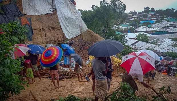 Onlookers stand as Rohingya refugees work amid the debris of houses in Balukhali camp that were damaged after monsoon rains triggered landslides and flash floods in the hilly settlements