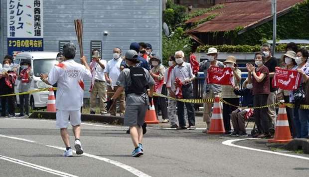 A torch bearer (L) running with the Olympic torch past spectators during the Tokyo 2020 Olympic Games Torch Relay in Yaizu, Shizuoka prefecture on June 24.