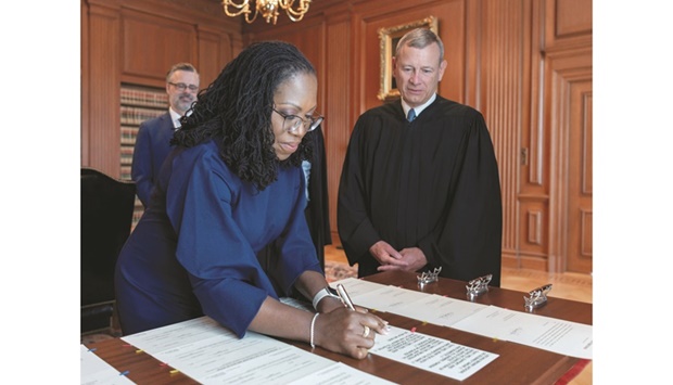 Justice Ketanji Brown Jackson signs her oaths of office as her husband Patrick and US Supreme Court Chief Justice John Roberts look on after she took her oath of office at the Supreme Court building in Washington yesterday. (Reuters)