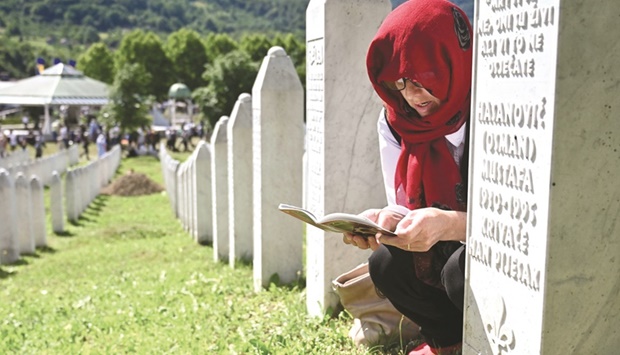 A Bosnian Muslim woman, a survivor of the 1995 Srebrenica massacre, reads from an Islamic prayer book near the graves of her relatives, at the memorial cemetery in the village of Potocari, near eastern Bosnian town of Srebrenica yesterday. (AFP)