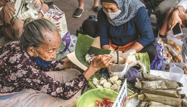 Septuagenarian Mbah Satinem (left) prepares lupis, a traditional sweet dish made from glutinous rice and served with grated coconut and liquid palm sugar, at her street stall in Yogyakarta.