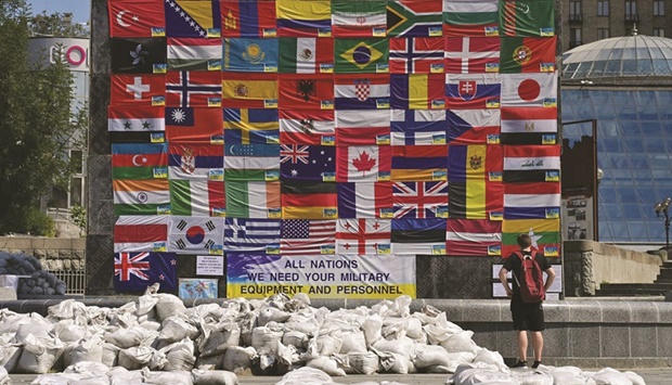A man stands past on the ground as he looks at a wall with flags from all over the world and a poster reading u201cAll nations, we need your military equipment and personnelu201d in Kyiv last week. (AFP)