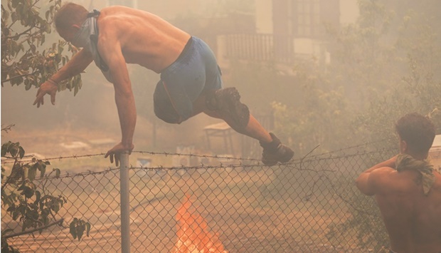 A local jumps over a fence as wildfire burns near the village of Vatera, on the island of Lesbos yesterday. (Reuters)