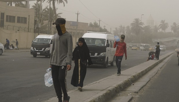 People walk in the street during a dust storm in the Iraqi capital Baghdad, on July 3, 2022.